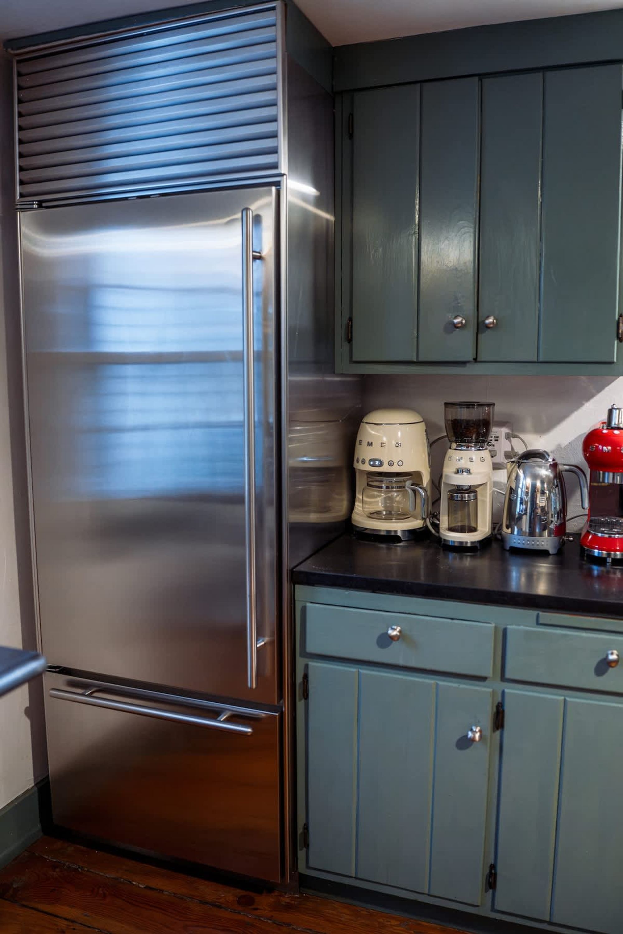 A stainless steel refrigerator, a coffee maker, and a red kettle on a kitchen counter.