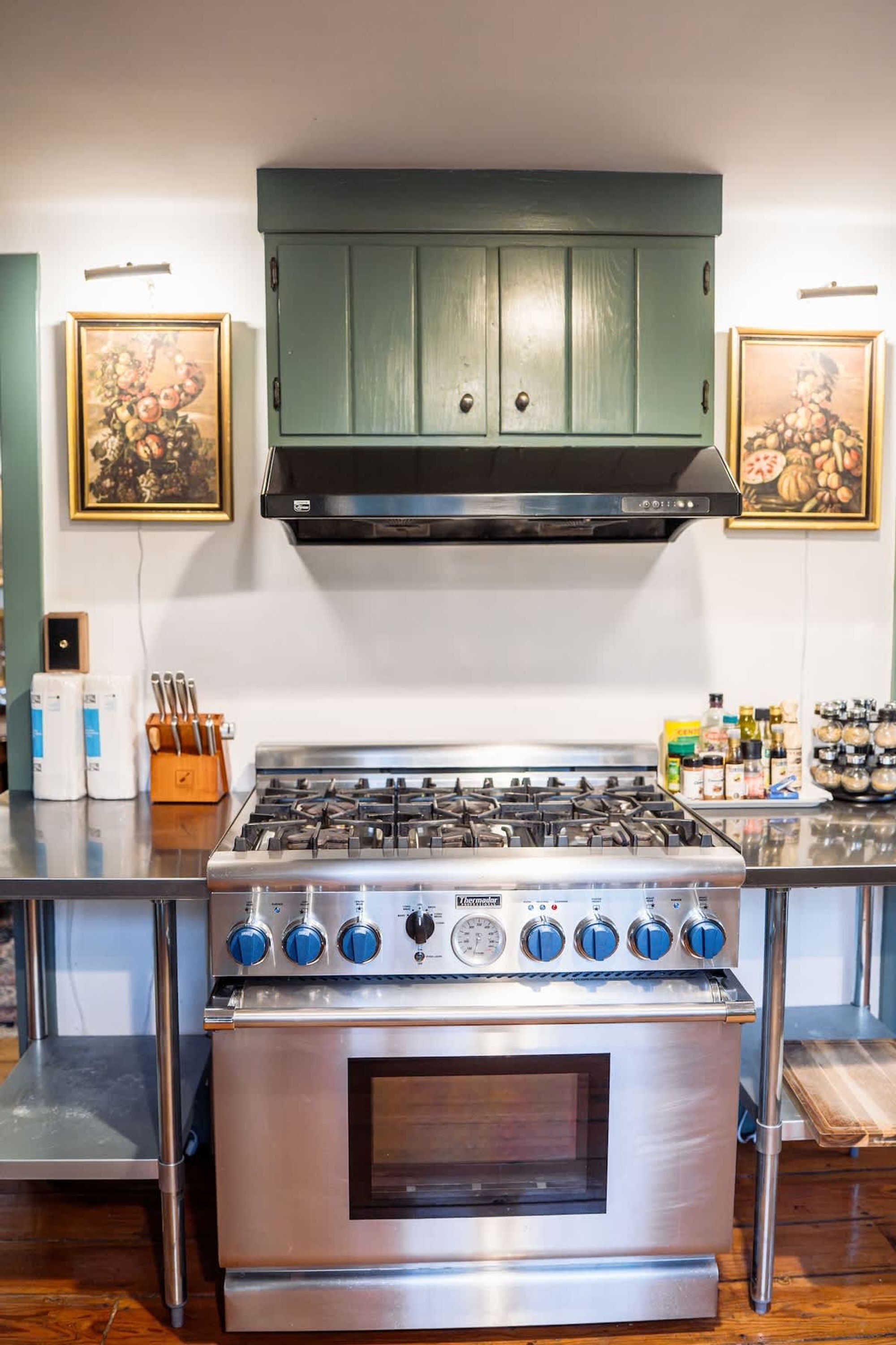 A kitchen with a stainless steel stove, a wooden cabinet, and two framed pictures on the wall.