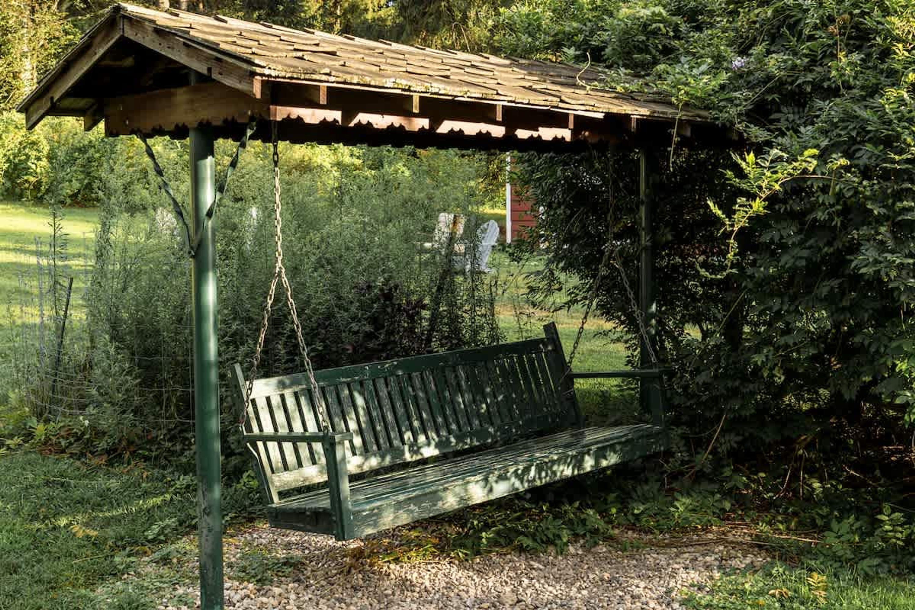 A rustic wooden bench under a metal shelter in a lush garden setting.