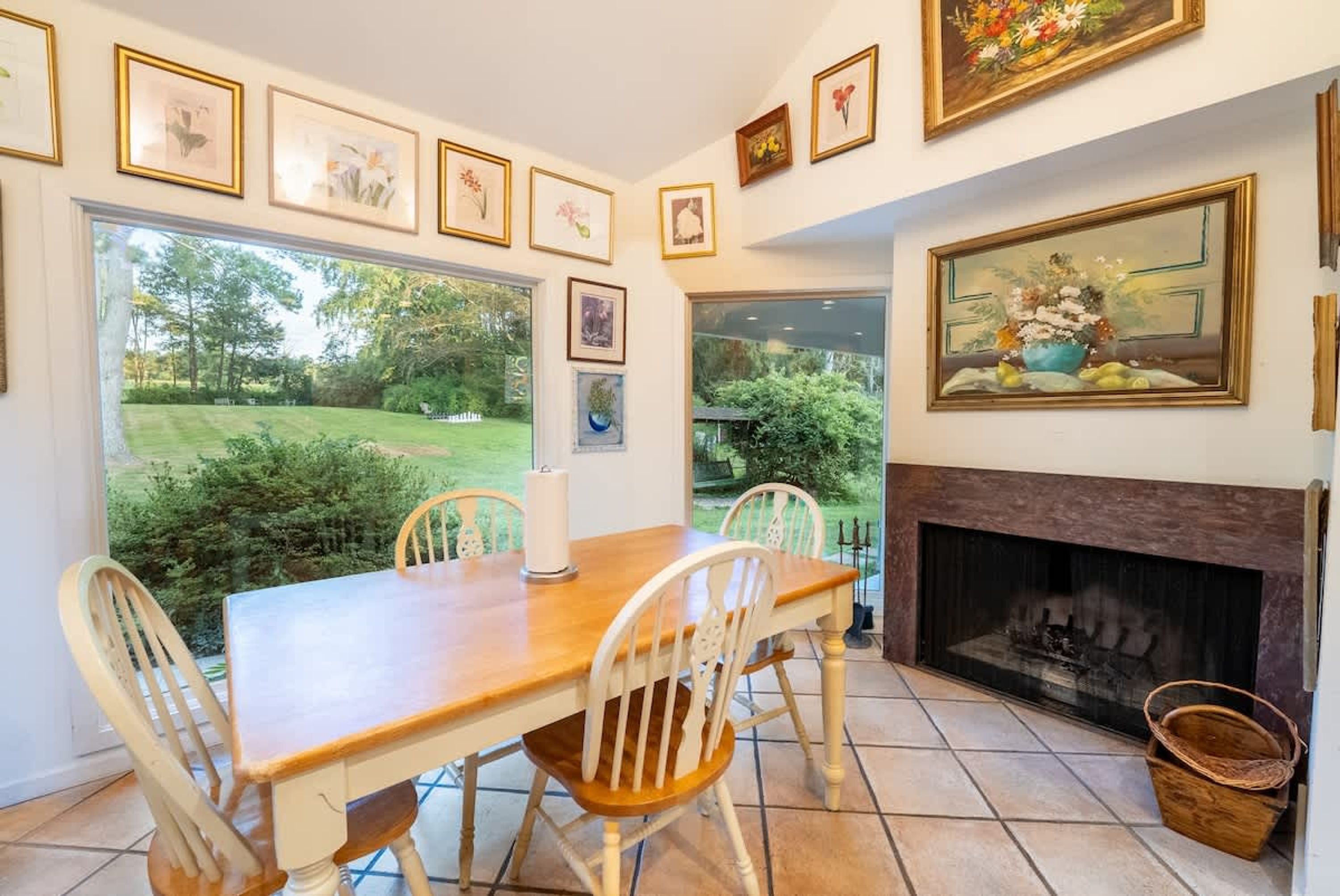 A dining area with a wooden table and chairs, a fireplace, and framed artwork on the walls.