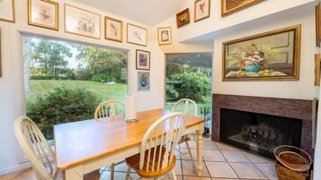A dining area with a wooden table and chairs, a fireplace, and framed artwork on the walls.