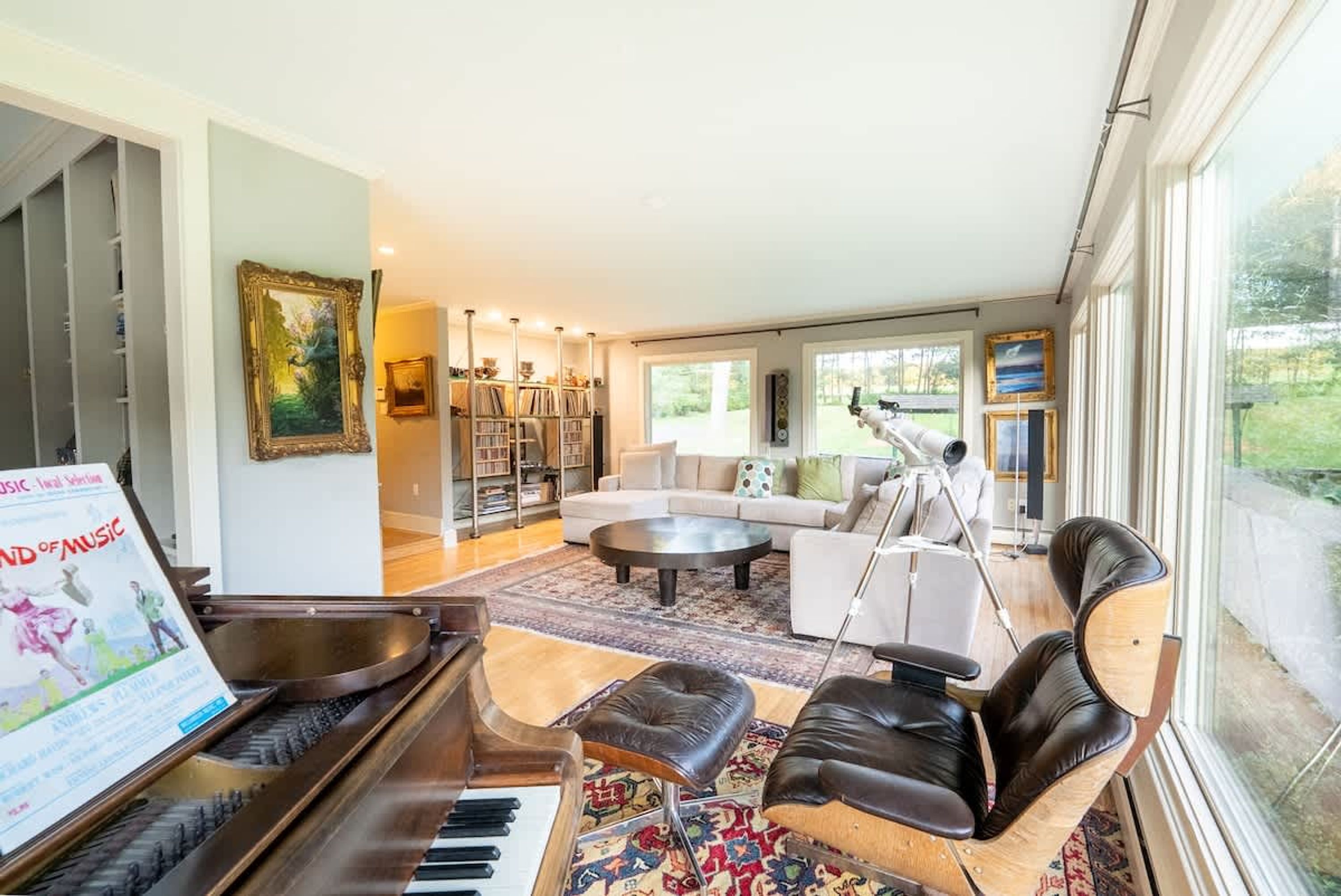 A spacious living room with a grand piano, a sofa set, and a large window offering a view of the outdoors.