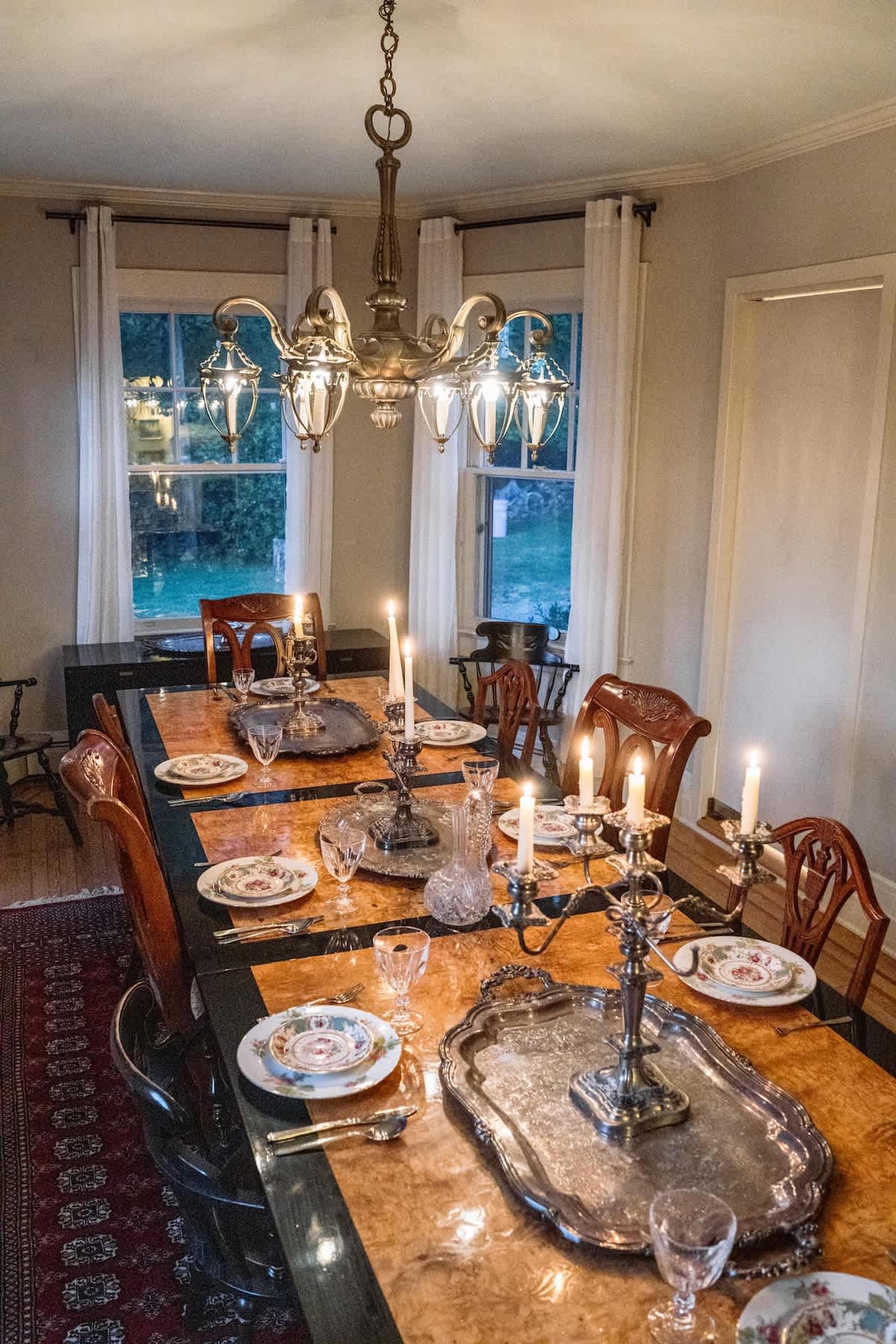 Een eetkamer met een lange tafel voor zes personen, inclusief een kroonluchter, kaarsen en uitzicht op het omliggende landschap.