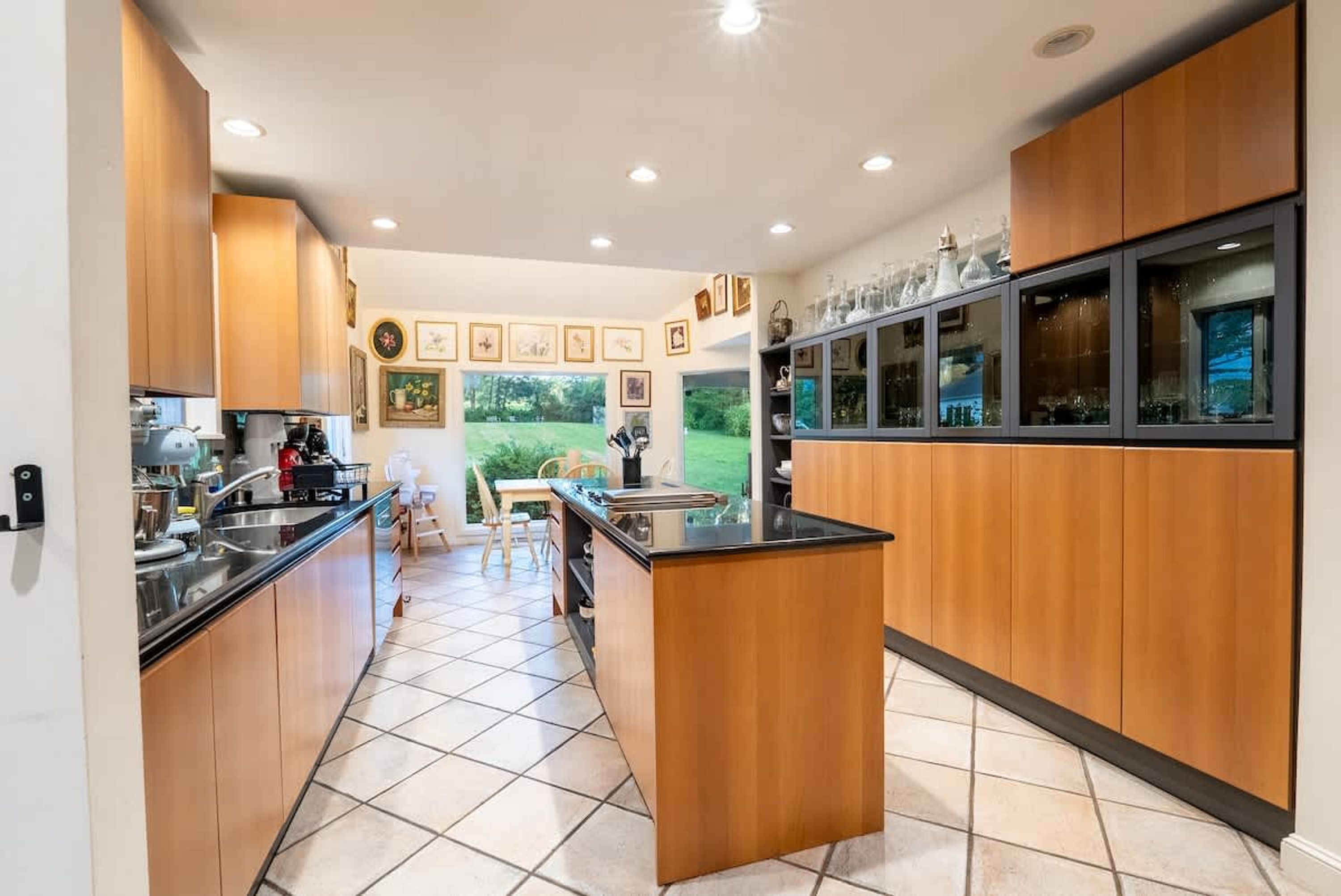 Una cocina moderna con armarios de madera, encimera negra y vista a un jardín a través de un ventanal grande.