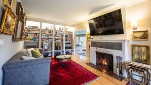 A living room with a fireplace, a large TV, and a bookshelf filled with books and decorative items. - Private Luxurious Canal Estate (Princeton)