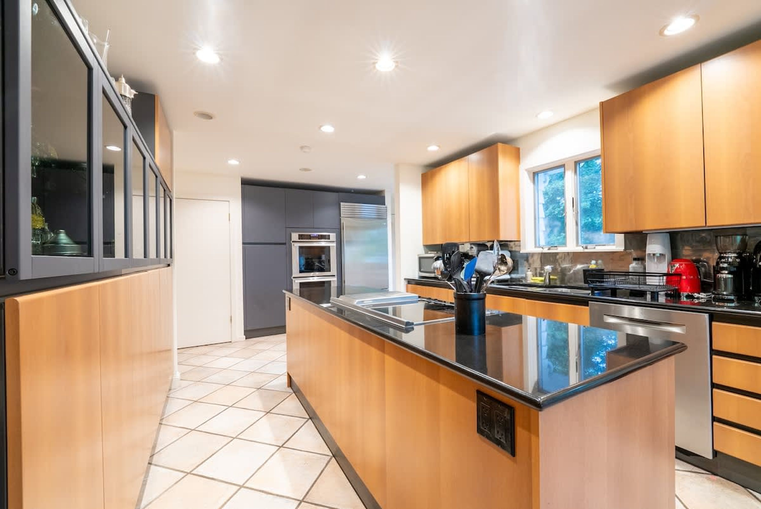 A modern kitchen with wooden cabinets, a central island, stainless steel appliances, and a tiled floor.