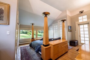 Une chambre à coucher avec un grand lit, des tables de chevet en bois, une commode et une vue sur un jardin par la fenêtre.