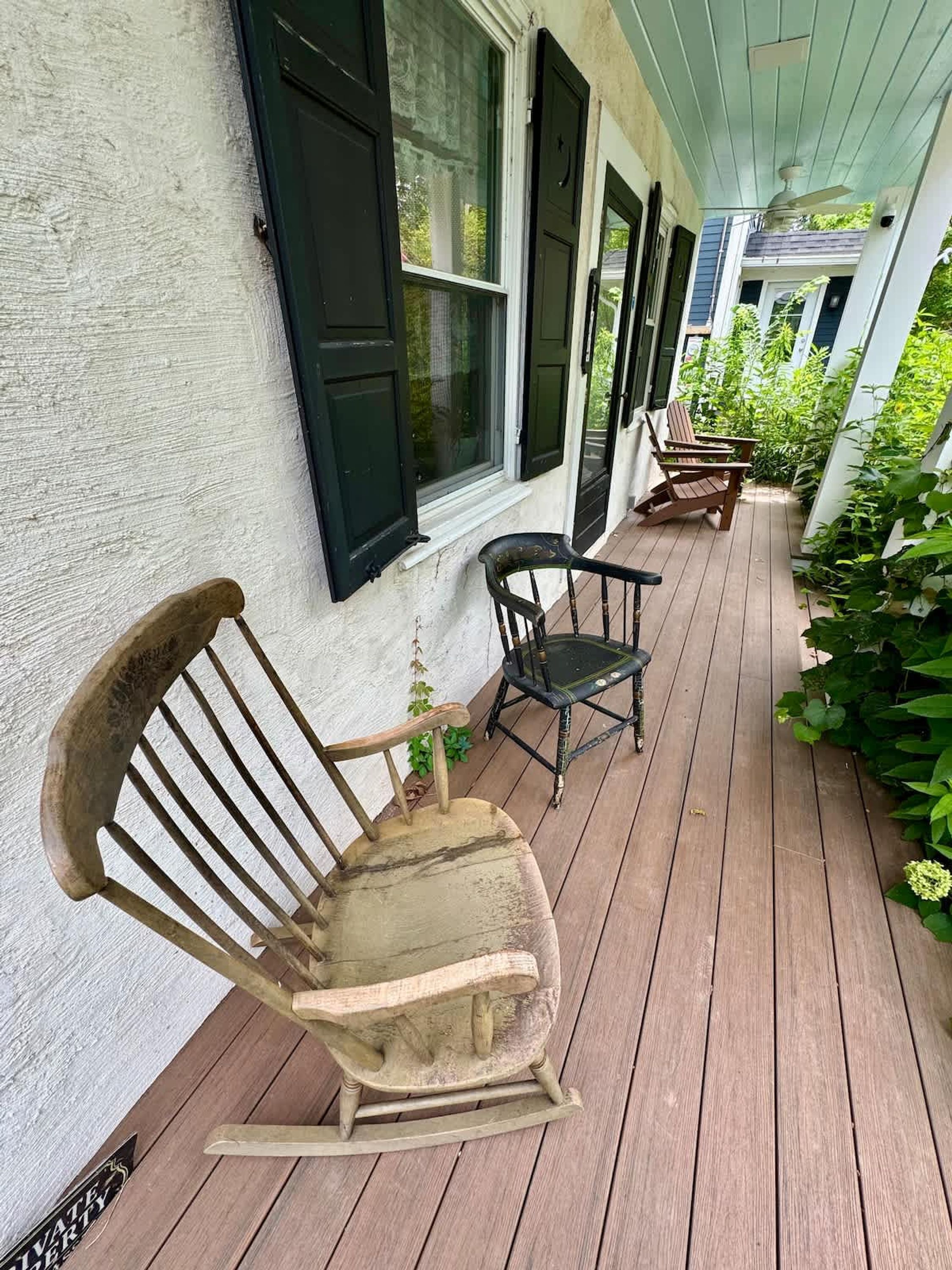A wooden porch with rocking chairs and a small table, surrounded by greenery.