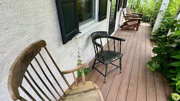 A wooden porch with rocking chairs and a small table, surrounded by greenery.