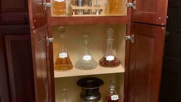 Un meuble en bois doté de plusieurs étagères, contenant divers objets en verre et bouteilles, notamment des verres à vin, des carafes et des bouteilles de whisky et de rhum.