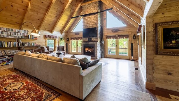 A cozy log cabin interior with a large sofa, bookshelves, a fireplace, and a high ceiling. - Private Luxury Log Cabin (New Hope)