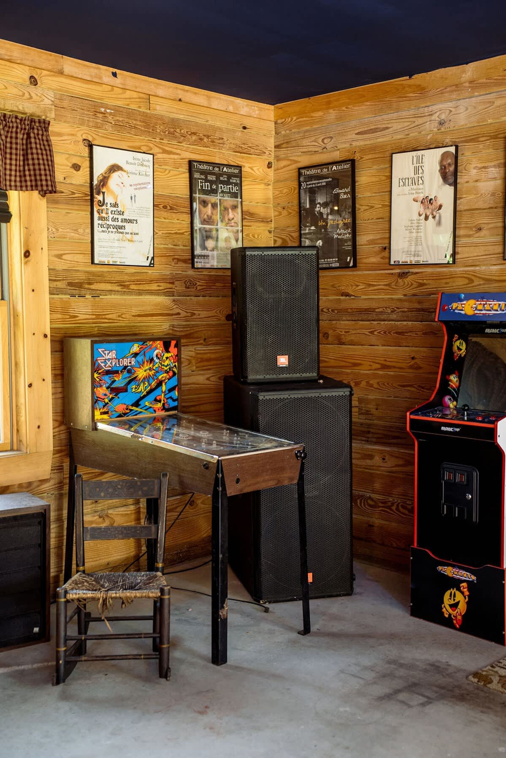 A room with wooden walls, a table with a Star Explorer game, a black speaker, and a red arcade machine.