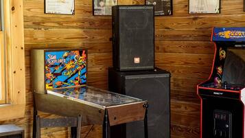 A room with wooden walls, a table with a Star Explorer game, a black speaker, and a red arcade machine.