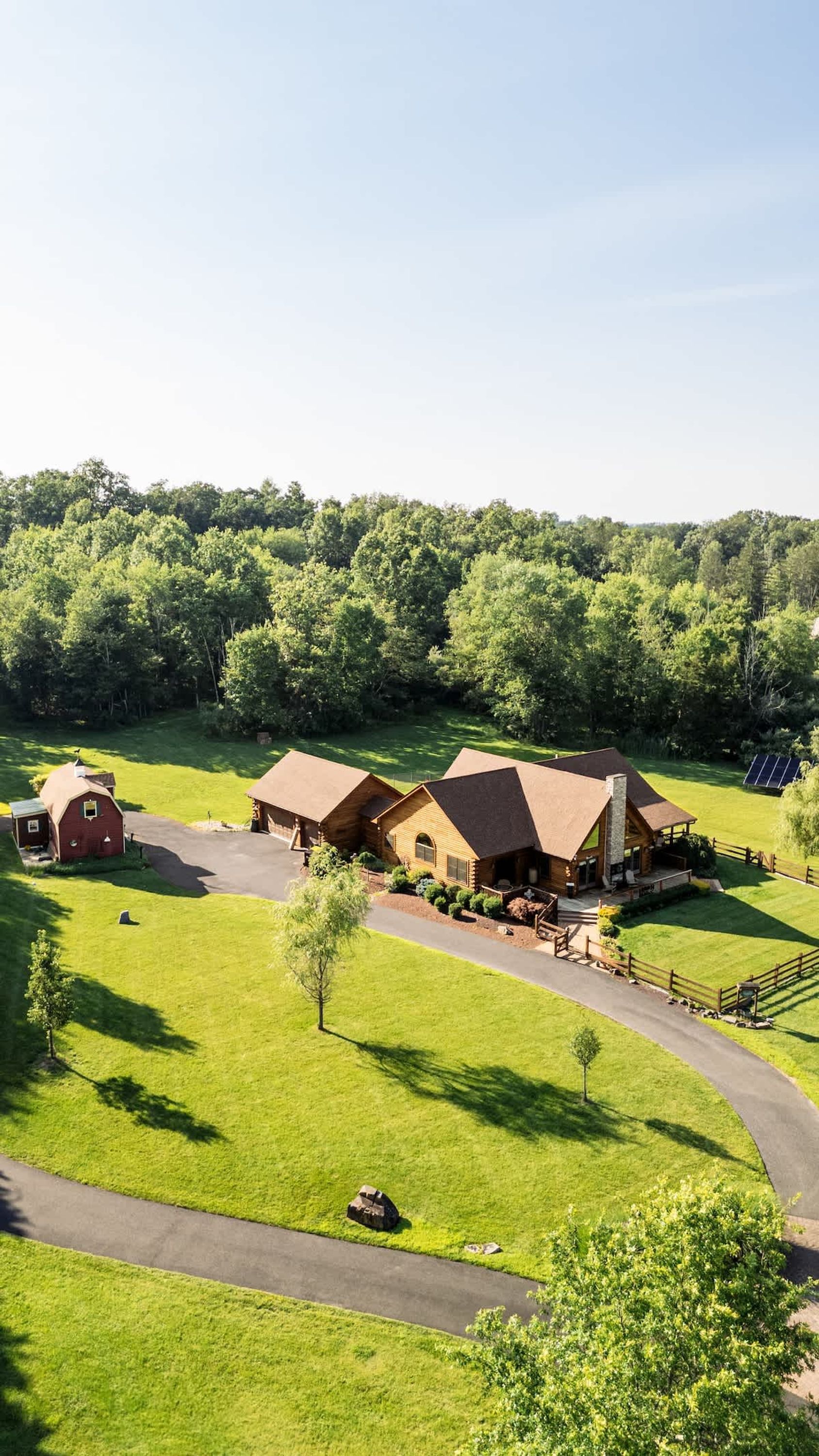 Un gran lodge rústico con varias cabañas y un granero, rodeado de extensos céspedes verdes y un bosque denso.