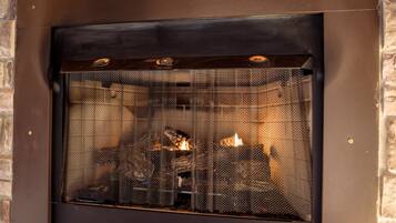 A fireplace with a metal screen, logs, and a brick wall.
