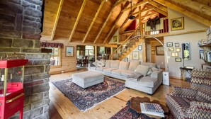 A spacious living room with a high wooden ceiling, a stone fireplace, and a staircase leading to an upper level. - Private Luxury Log Cabin (New Hope)