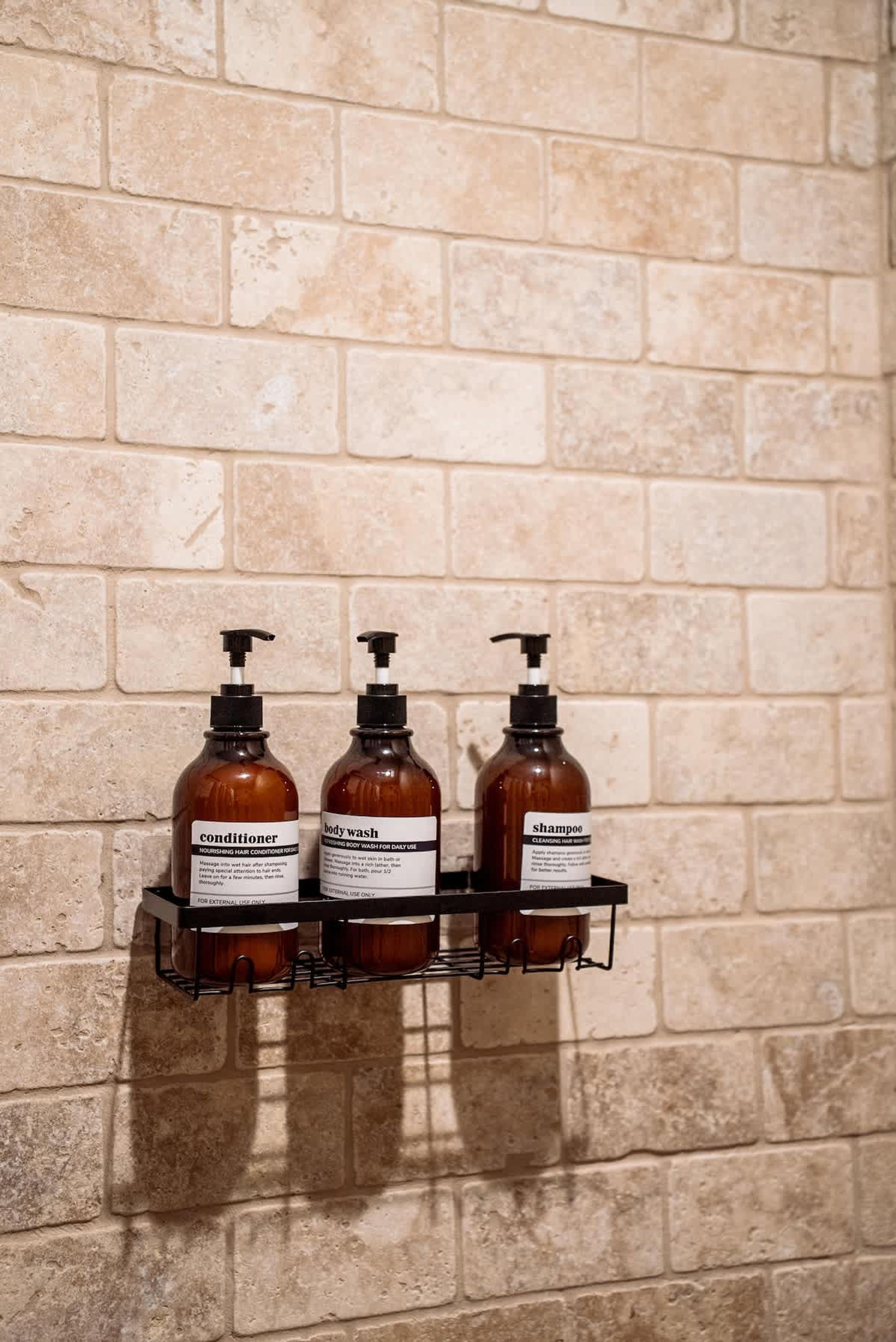 A wall-mounted shelf with three bottles of toiletries against a brick wall.