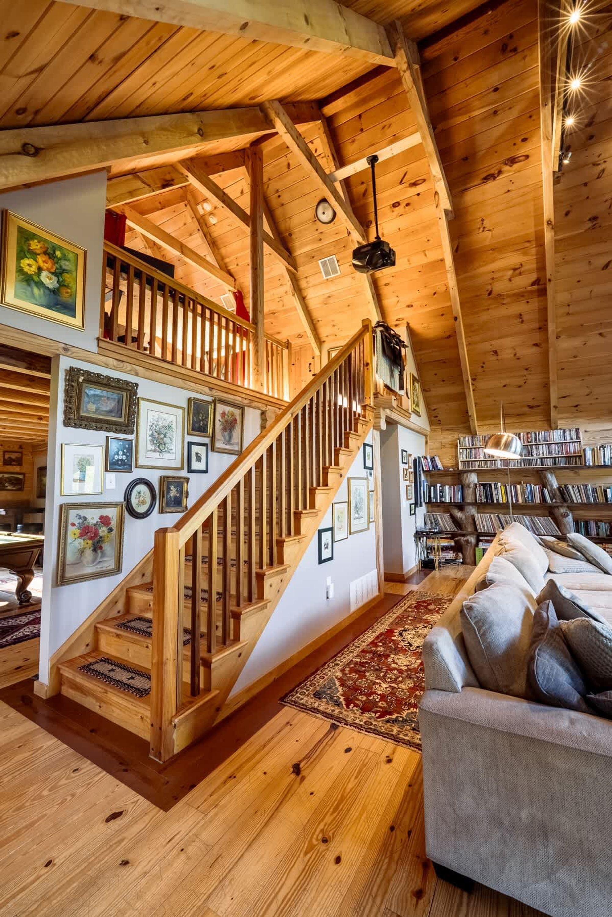 Un loft amplio con una escalera de madera, una zona de estar acogedora con un sofá y una estantería llena de libros.