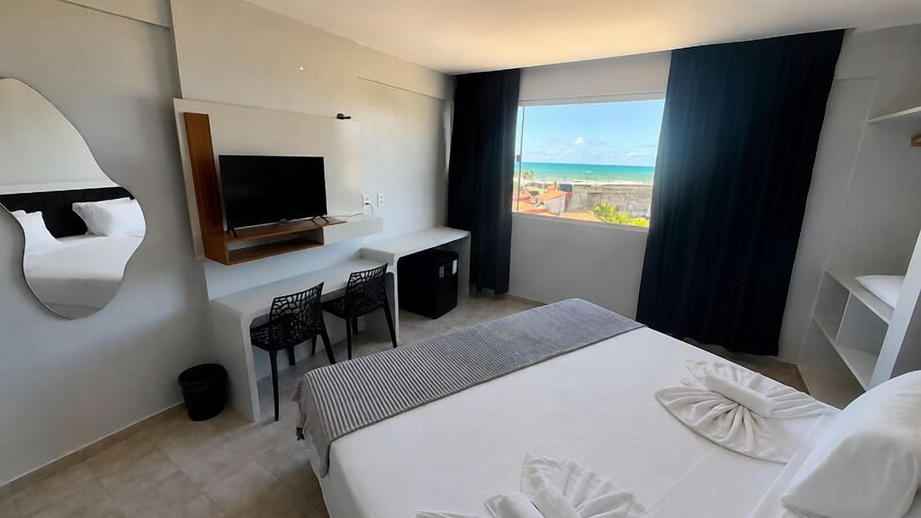 Une chambre d’hôtel avec un lit, un bureau et une chaise, une télévision et une vue sur la plage.