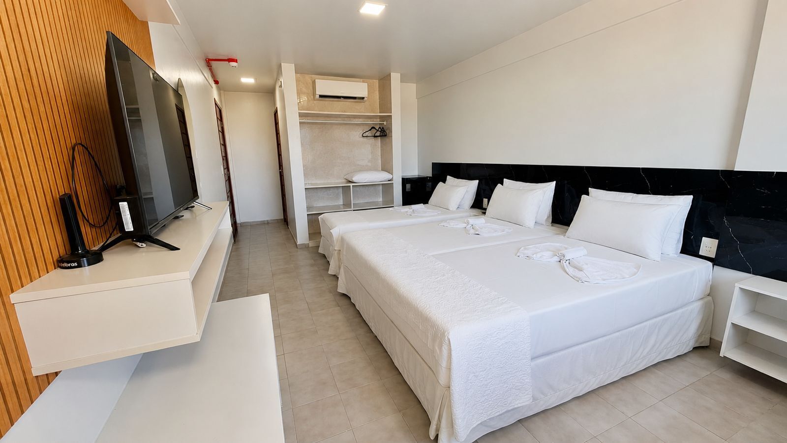 Habitación de hotel con televisión, cama con ropa blanca, armario y espejo.