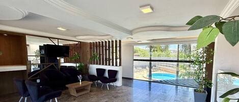 A modern lobby with a pool view, dark furniture, and a TV.