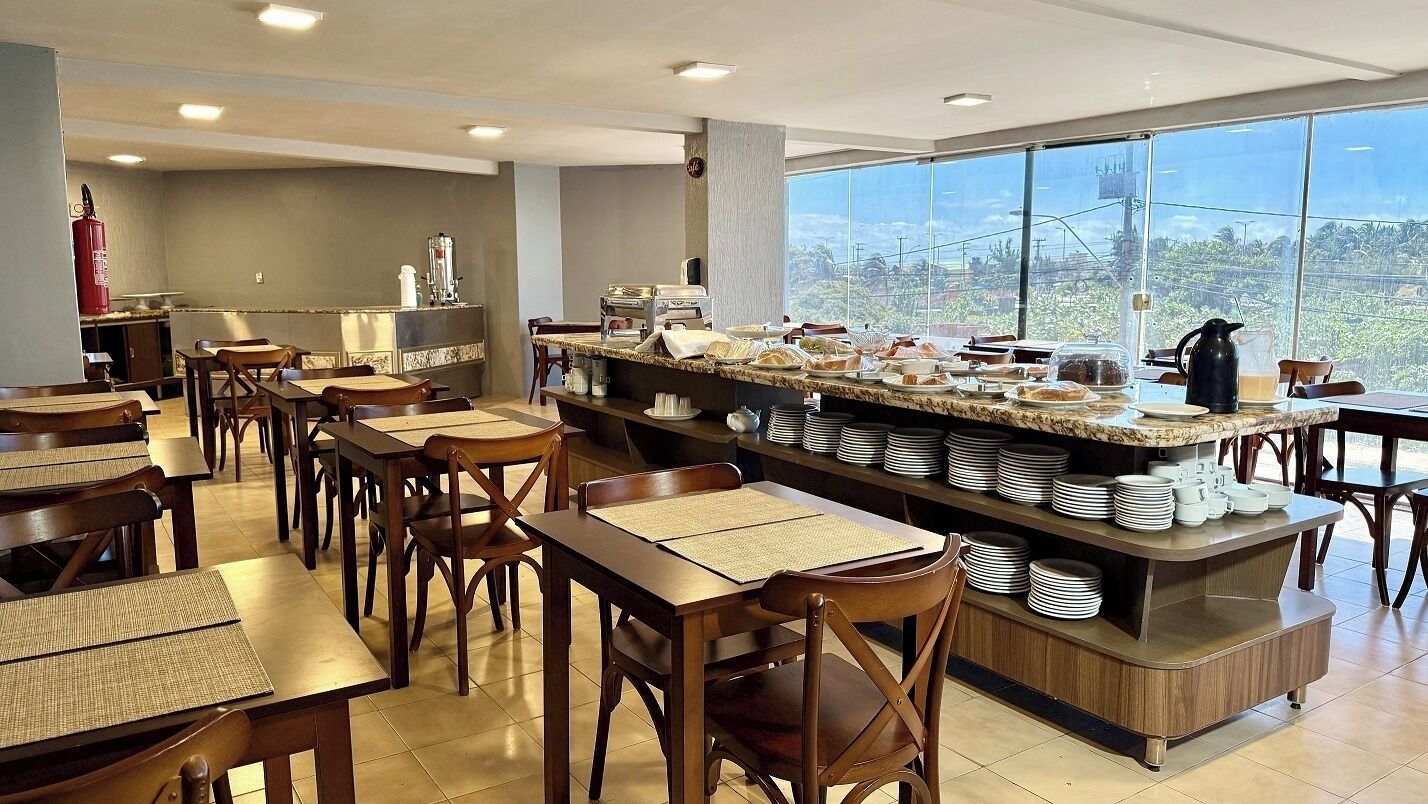 A restaurant with multiple tables and chairs, a buffet counter with various food items, and a large window offering a view of the outdoors.