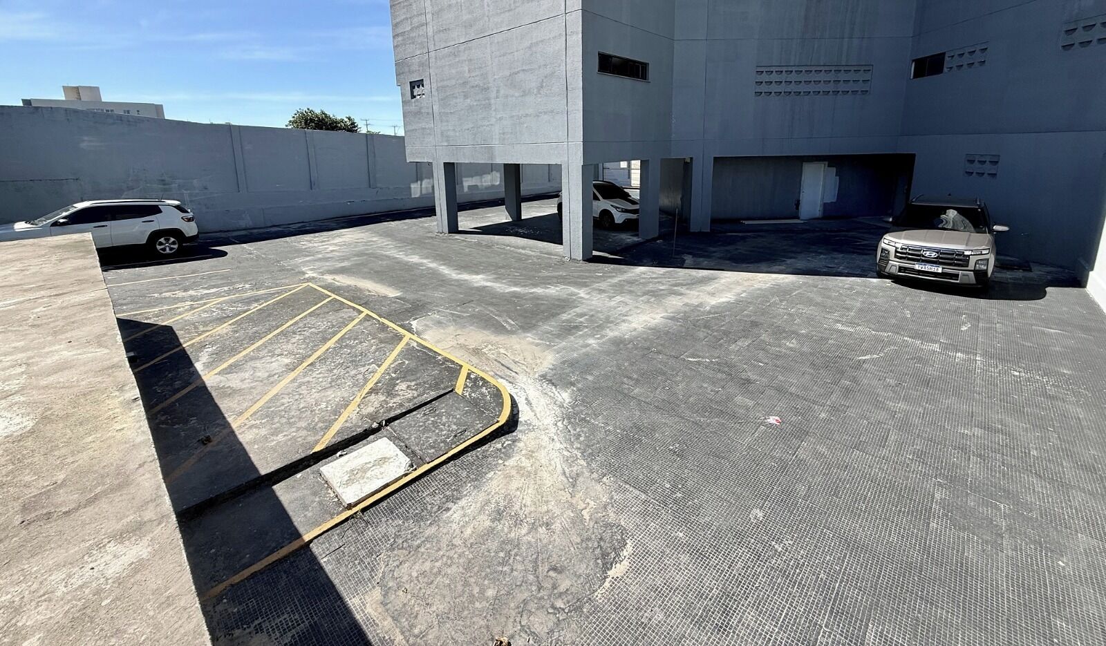 A parking area with concrete structures, a white car, and a building with a flat roof.