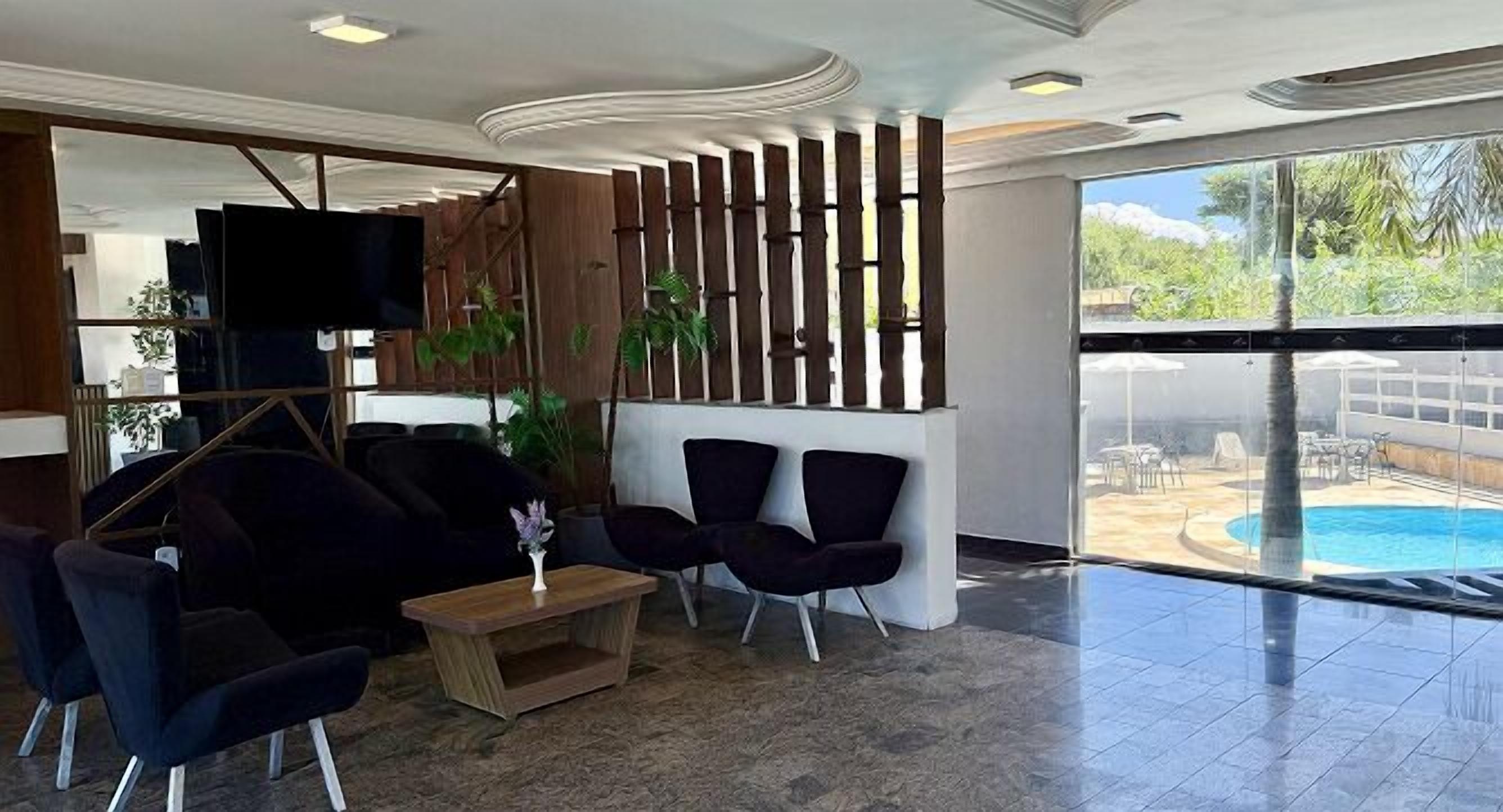 A modern lobby with dark sofas, a wooden partition, a flat-screen TV, and a view of an outdoor pool.