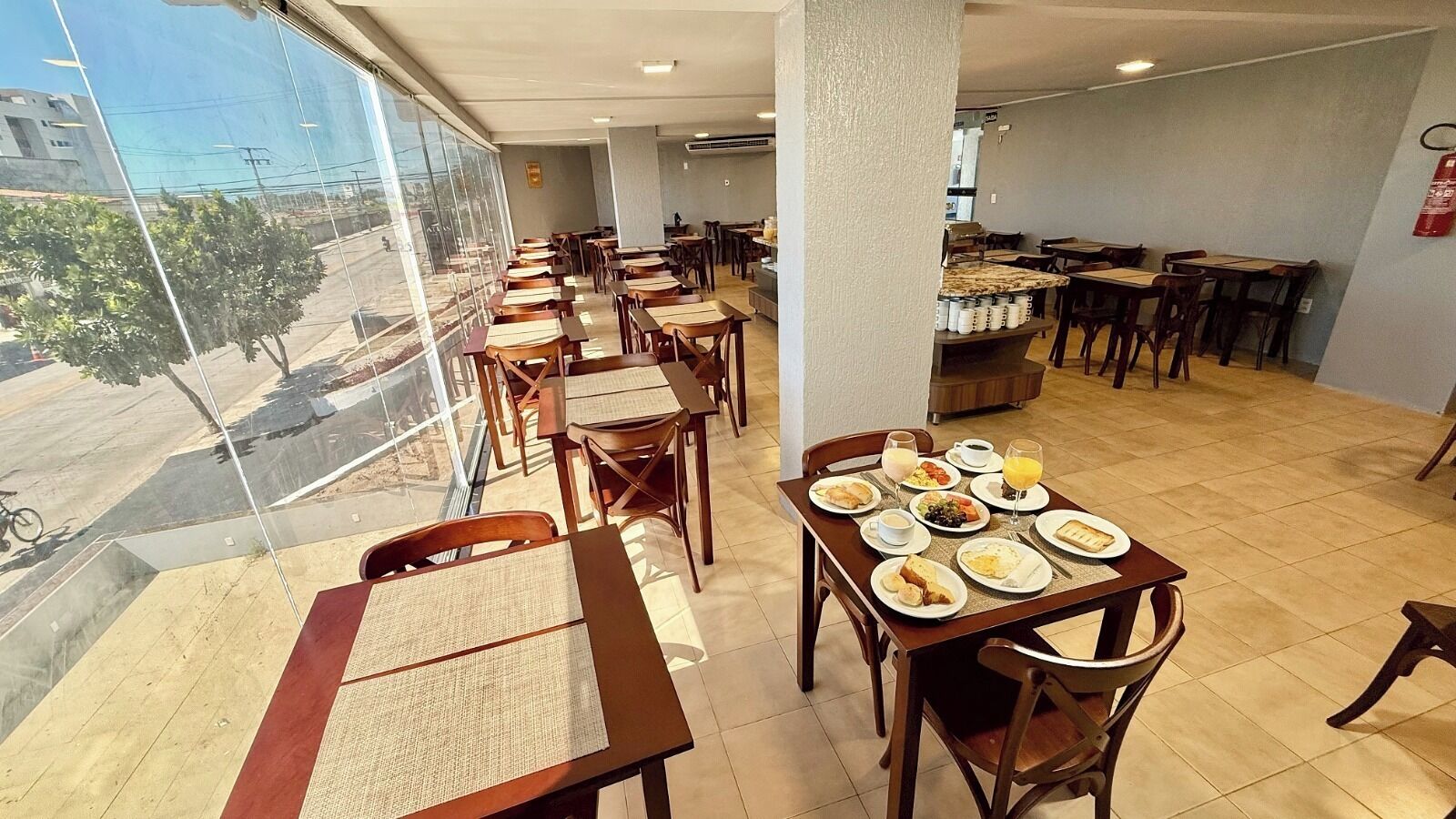Ein Restaurant mit gedeckten Tischen für das Frühstück, einem an der Wand befestigten Feuerlöscher und Blick auf die Straße.