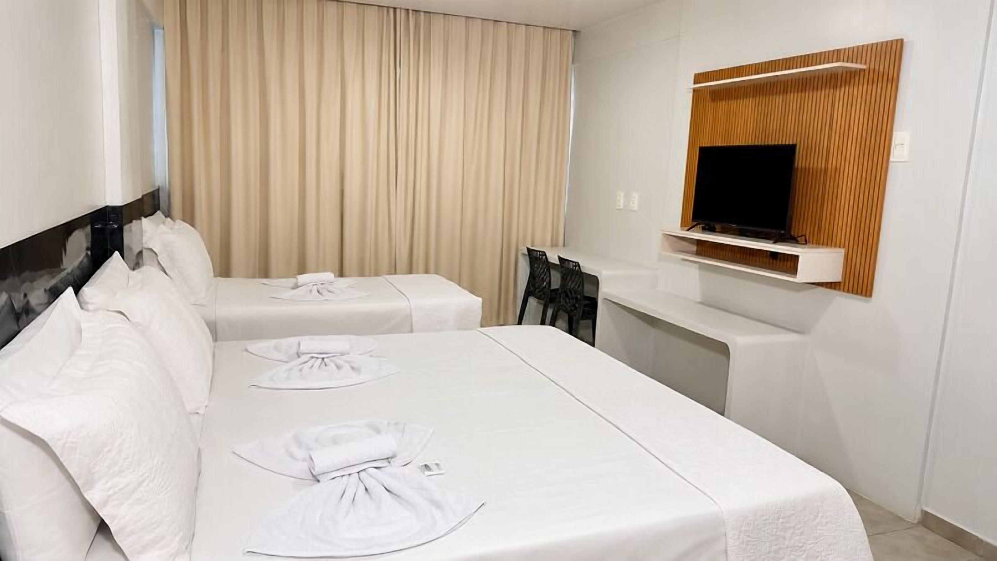 A hotel room with two beds, a TV, a desk, and a chair.