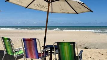 Cena de praia com um guarda-sol e três cadeiras de praia coloridas.