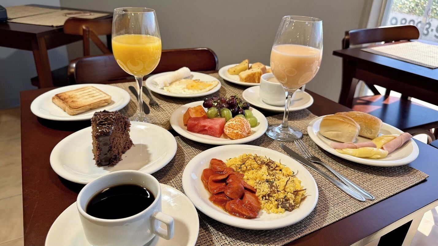 A breakfast setting with plates of food, two glasses of orange juice, a cup of coffee, and a wine glass.