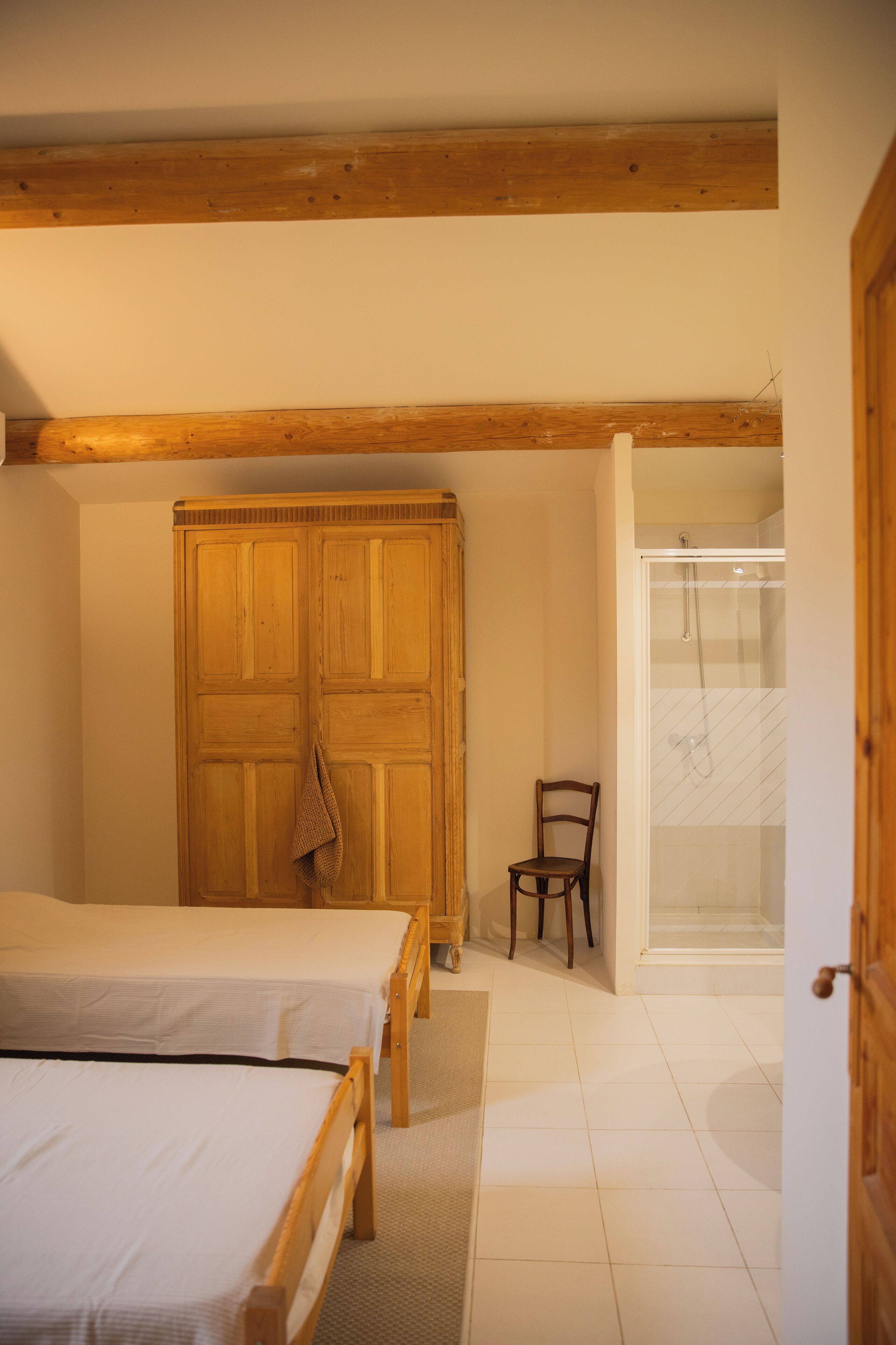 Un dormitorio con dos camas de madera, un armario de madera, una silla y una zona de ducha.