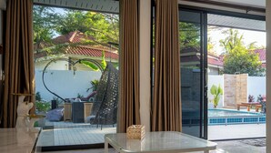 Une chambre moderne avec une table en verre, de grandes fenêtres et une vue sur une piscine et la verdure environnante.