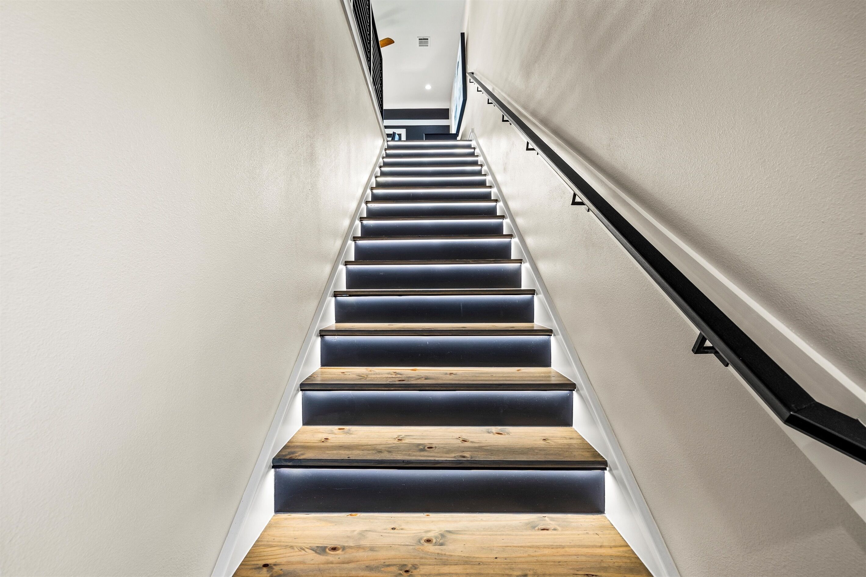 A modern staircase with wooden steps and black handrails, leading to a landing with a light fixture.