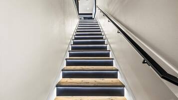 A modern staircase with wooden steps and black handrails, leading to a landing with a light fixture.