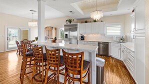 A spacious kitchen with a large island, wooden chairs, and white cabinetry. - Lux West End Retreat |Fire Pit, 210 Steps to Beach (Galveston)