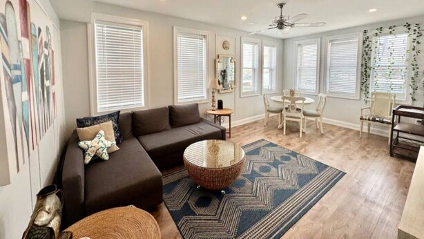 A spacious living room with a brown sofa, a round coffee table, and a dining area with white chairs. - 7 mins walk to Boardwalk & Beach! AC & Beach Tags! (Ventnor City)