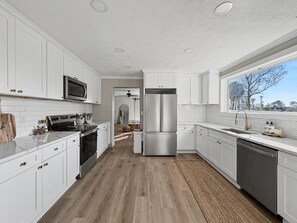A modern kitchen with white cabinetry, stainless steel appliances, and a wooden floor. - New! Walk to Augusta National 4BR Luxury Home with Air Condition (Augusta)