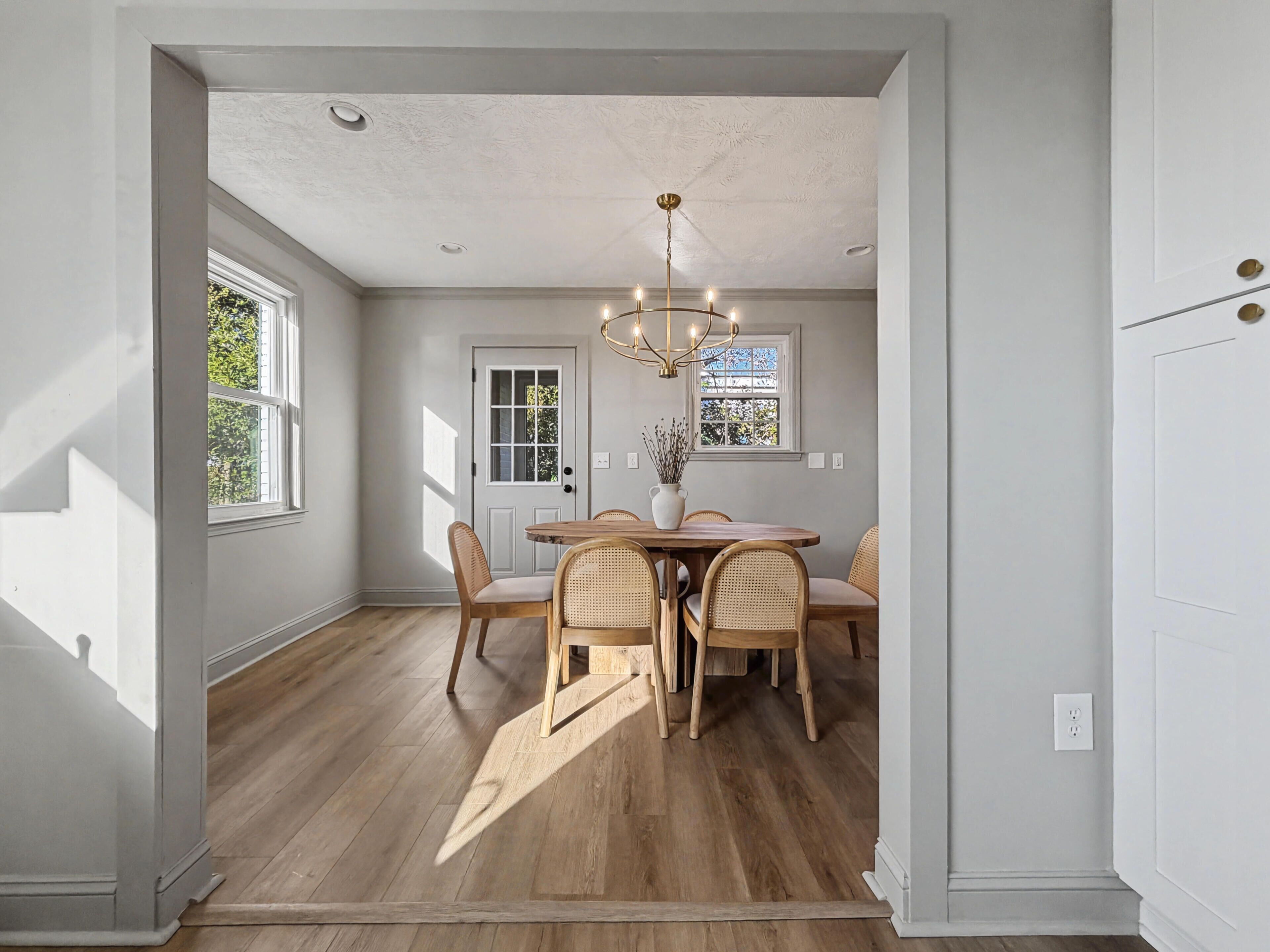 A dining area with a wooden table and chairs, a chandelier, and a view of the outdoors through large windows.