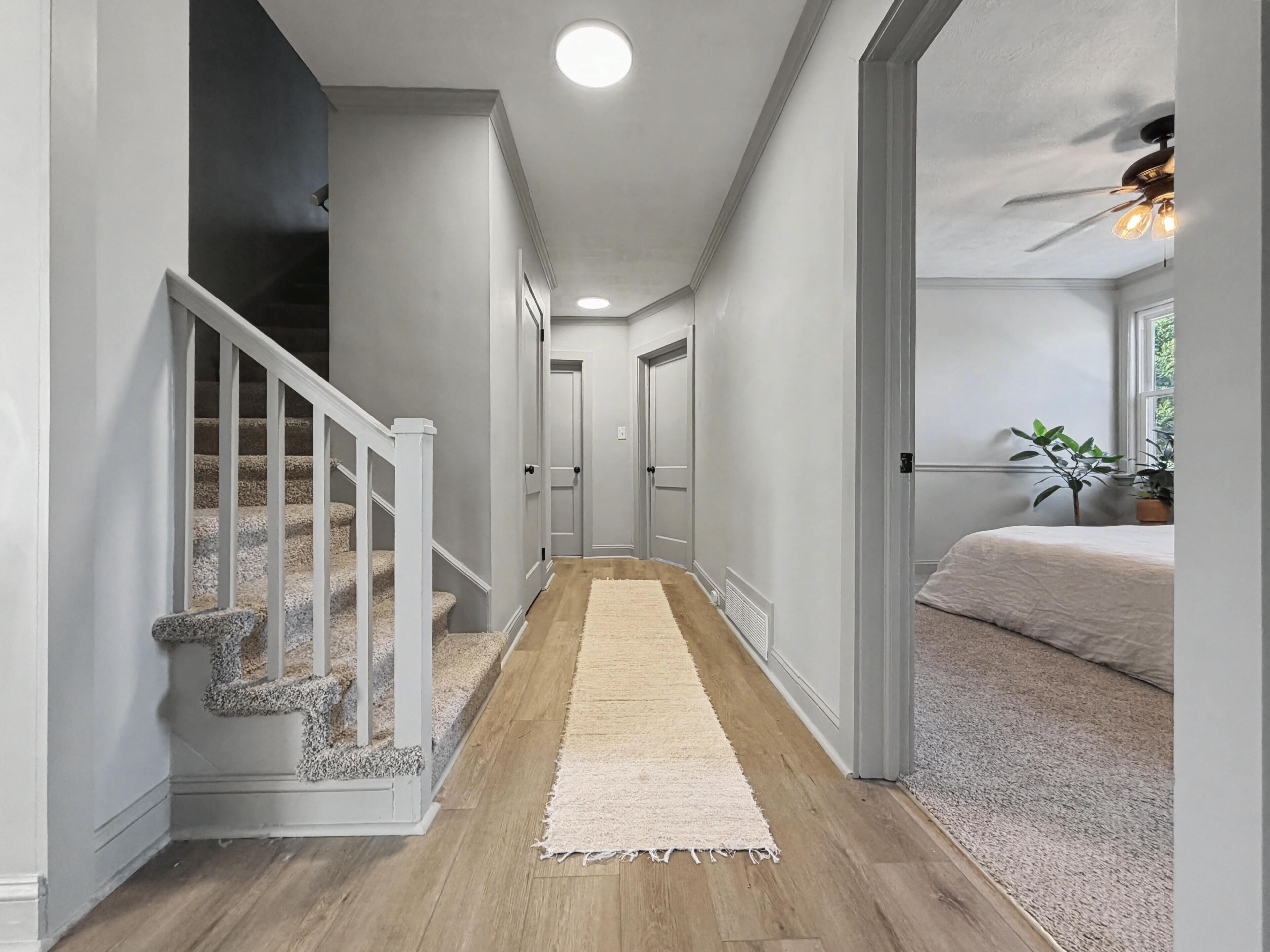 Un couloir doté d’un plancher en bois, de murs blancs, d’une moquette blanche et d’un escalier agrémenté d’éléments en pierre.