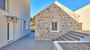 A stone building with a sloped roof and a window, adjacent to a modern building with a glass balcony. - Hedera Estate, House Hedera III (Dubrovnik)