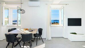 A modern room with a dining table, chairs, a pendant light, a flat-screen TV, and a view of the sea. - Hedera Estate, House Hedera III (Dubrovnik)