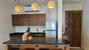 Una cocina moderna con una isla central, taburetes de madera, un refrigerador de acero inoxidable y lámparas colgantes.