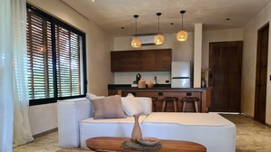Una sala de estar moderna con un sofá, una mesa de centro de madera y una cocina con armarios de madera y un refrigerador.