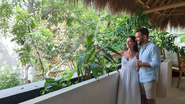 Una pareja de pie en un balcón con vistas a abundante follaje y una estructura de techo de paja.