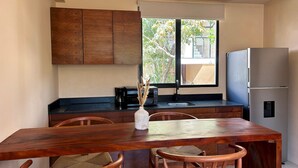 Una cocina moderna con armarios de madera, un refrigerador de acero inoxidable, una mesa de comedor con dos sillas y una ventana con vista a árboles.