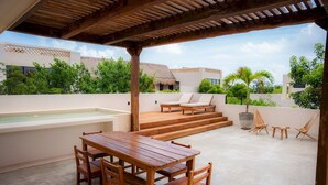 Un patio exterior de madera con una mesa y sillas, un jacuzzi y sillones de descanso.