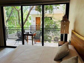 A bedroom with a large window, a bed, a nightstand, and a view of a balcony with a table and chairs. - Jungle View Studio S19 Private Balcony Hammock Pool (Tulum)