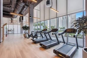 A modern gym with treadmills, exercise bikes, and a large window offering a city view. - Vogue | Forte Downtown near Dubai Mall | Burj Khalifa (Dubai)